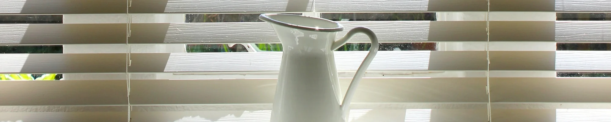 Water pitcher sitting on a table in front of a window with blinds